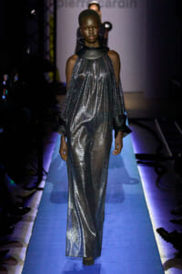 Fashion model on a runway wearing a metallic silver halter dress with a large black neck collar and matching wide black cuffs.