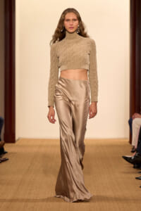 Model walks the runway in a beige cropped knit turtleneck and satin wide-leg trousers.