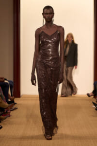 Model walks the runway in a floor-length, brown sequin gown with thin straps and dangling earrings.