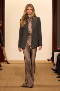 Model walking the runway in a charcoal pinstripe blazer over a taupe satin shirt and matching wide‑leg satin pants with a brown belt.