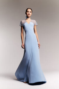 Model wearing a pale blue, floor-length satin gown with sheer dotted short sleeves and a matching choker, posing against a neutral backdrop.