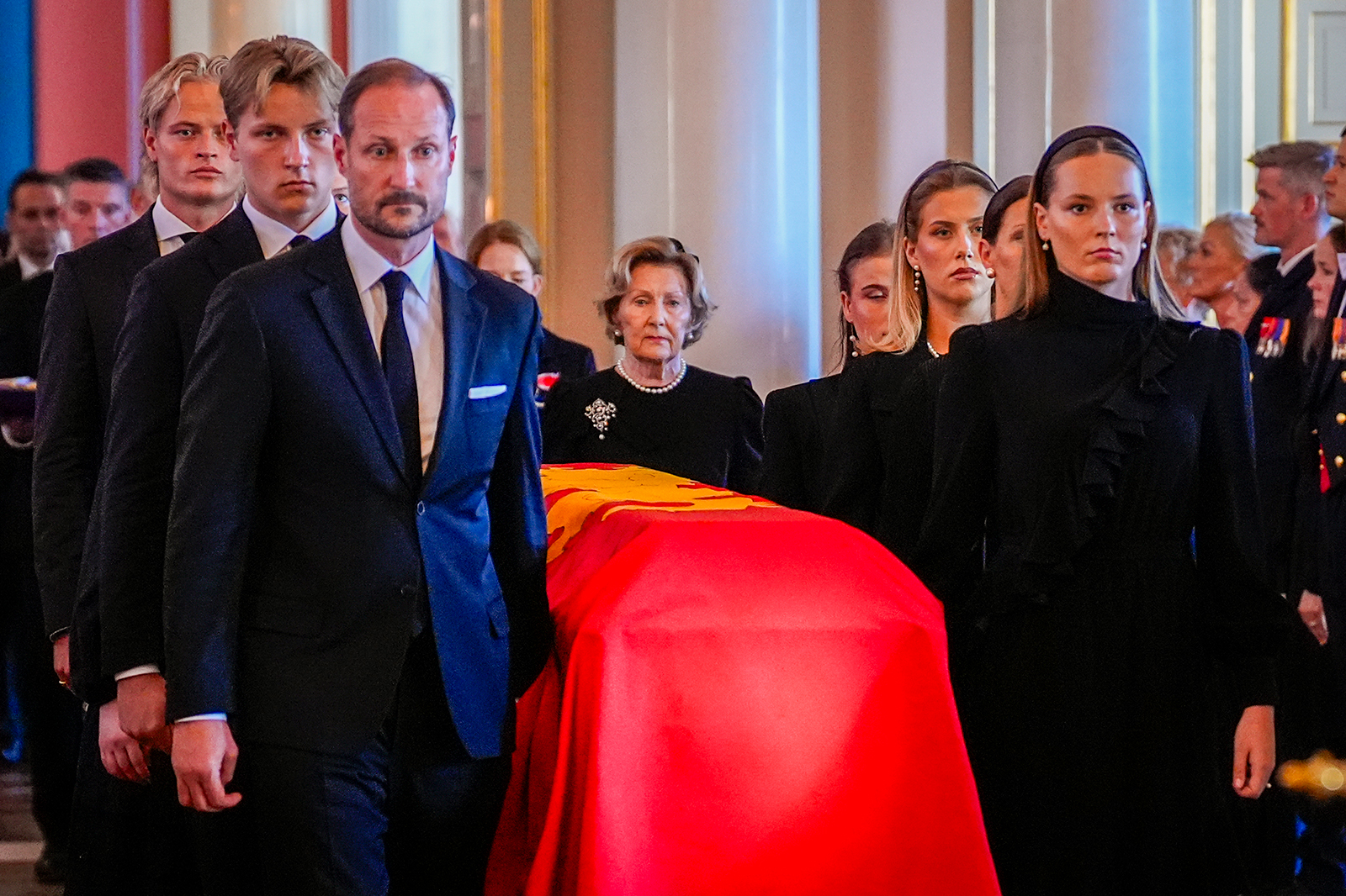 ノルウェー王室の紋章入りの赤い布で覆われたハーラル5世国王の柩に付き添い、王宮内を進むホーコン国王と喪服姿の王室メンバーたち