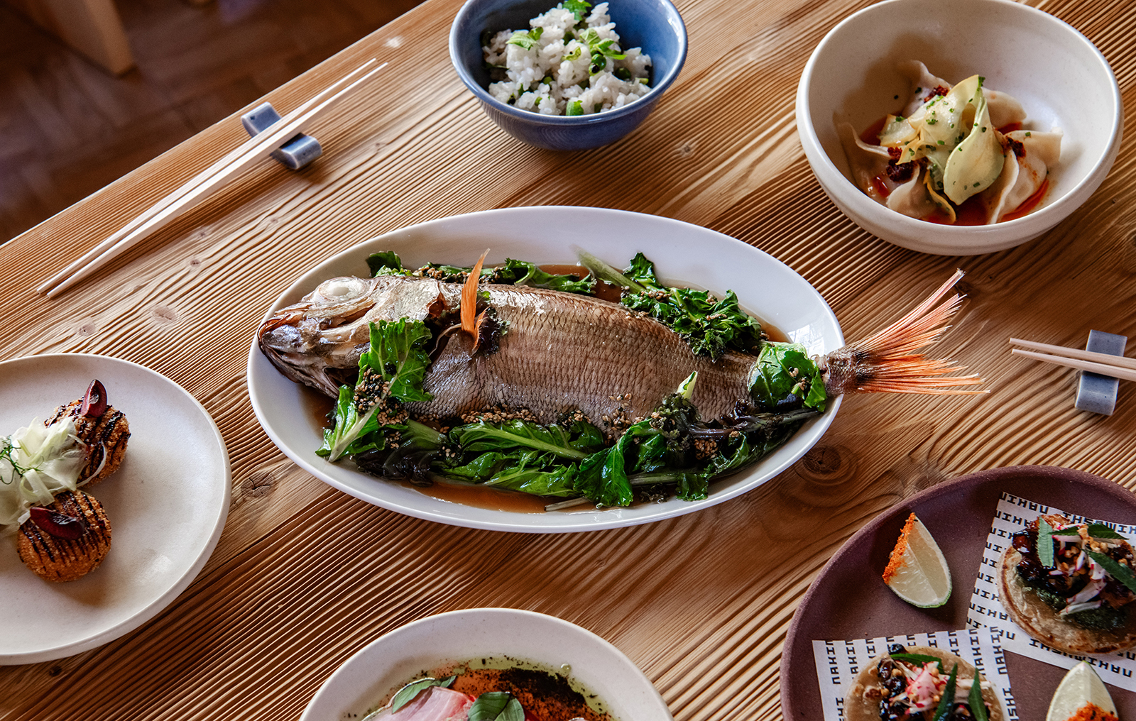 261006-DSC_8834 | madameFIGARO.jp(フィガロジャポン) 木のテーブルに並ぶ、ハーブを添えた魚の丸焼きや小鉢、タコスなど「ナキムシ」2階の料理