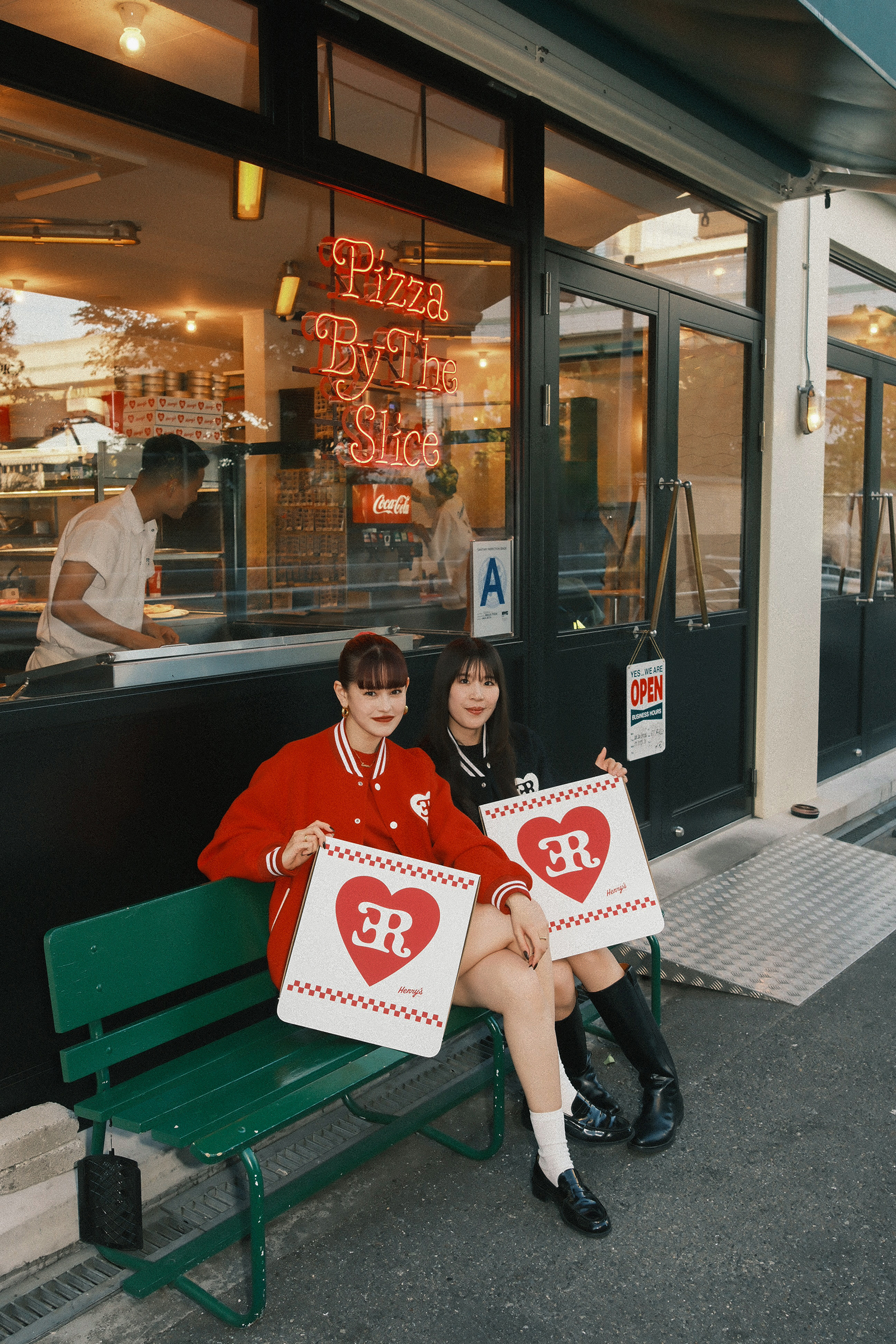 大阪のヘンリーズ ピザの店先のベンチに座り、ハートロゴ入りのピザボックスを手にするemmaと中村璃乃